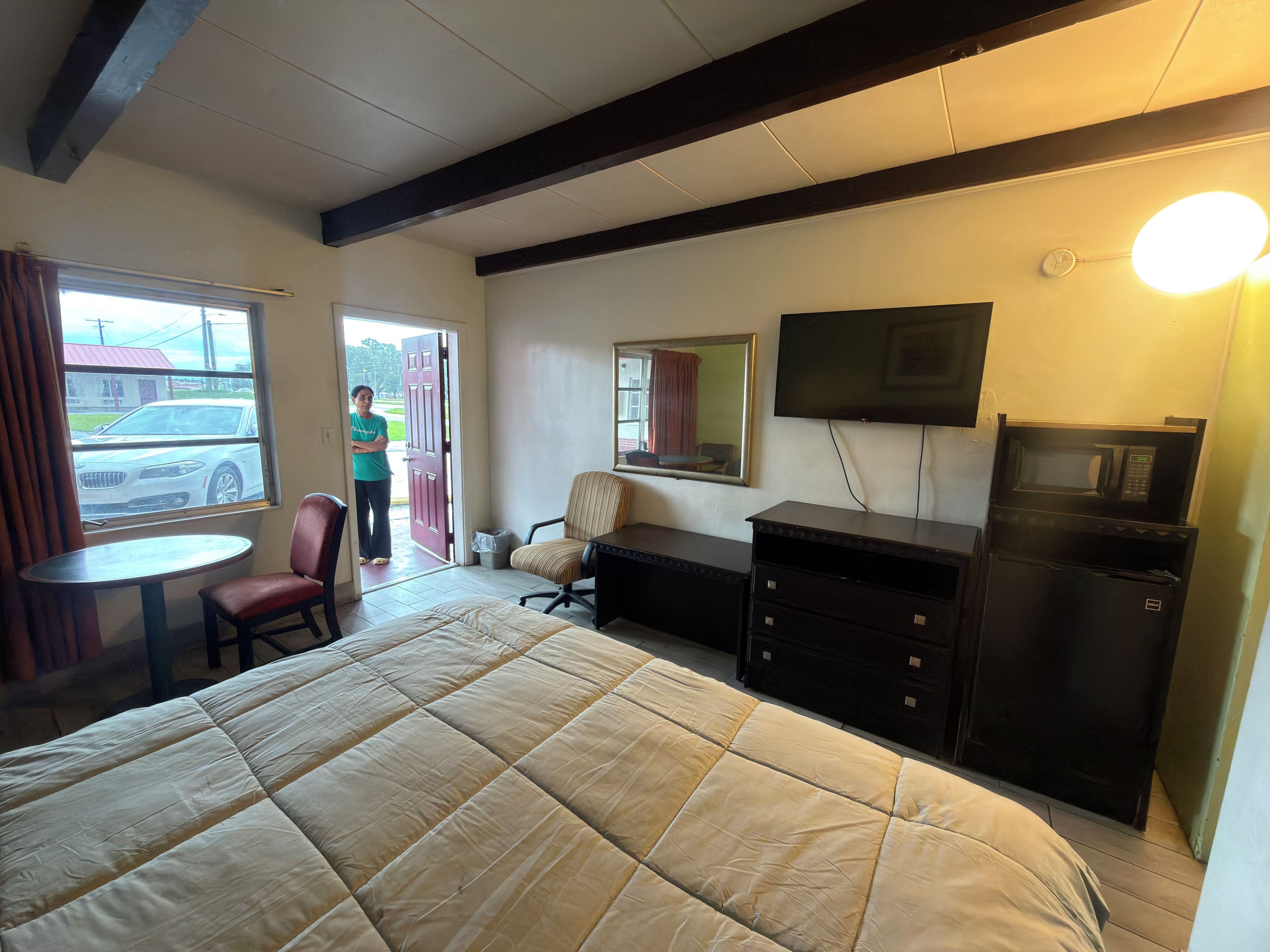 Habitación de hotel con cama, escritorio, silla, televisor y ventana con vista a un coche fuera.