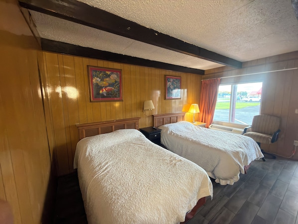 Une chambre d’hôtel avec deux lits, un mur en bois, un tableau, une fenêtre avec des rideaux et une chaise.