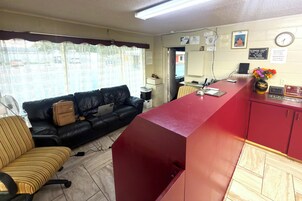 Una habitación con un mostrador de recepción rojo, un sofá de cuero negro, una silla a rayas y una computadora portátil sobre el sofá.