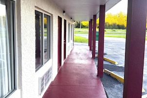 A covered walkway with windows and a red floor, leading to a parking area.