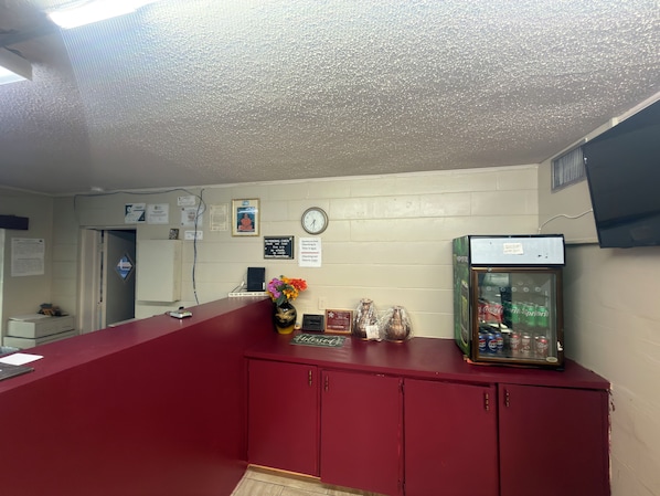 A reception desk with a clock, a refrigerator, and a vending machine.