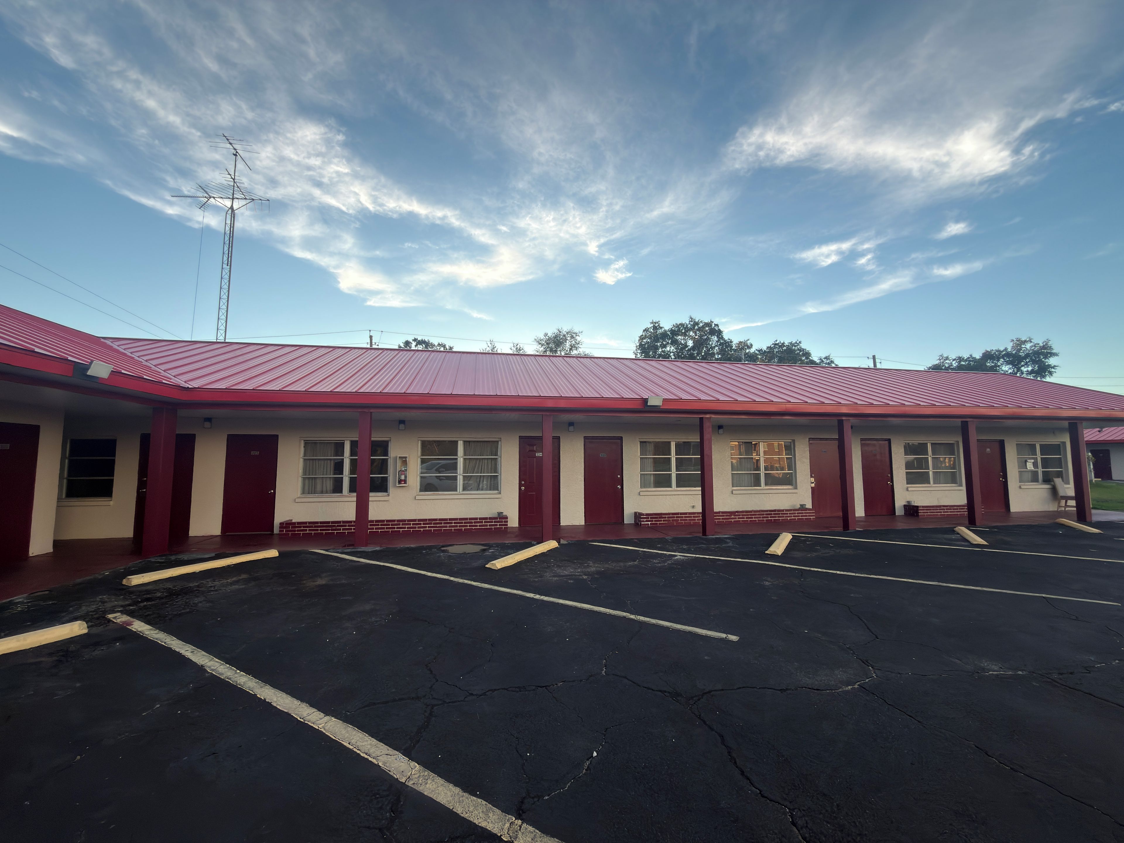 Un motel con techo rojo, varias habitaciones y un estacionamiento.