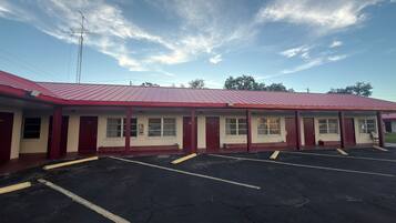 Un motel con techo rojo, varias habitaciones y un estacionamiento.