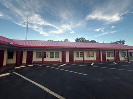 Un motel con techo rojo, varias habitaciones y un estacionamiento.