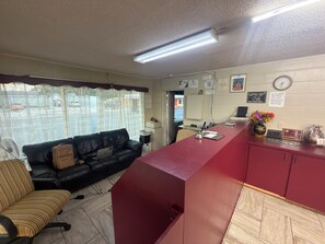 Zona de recepción de un hotel con un escritorio rojo, un sofá de cuero negro y una ventana con cortinas.