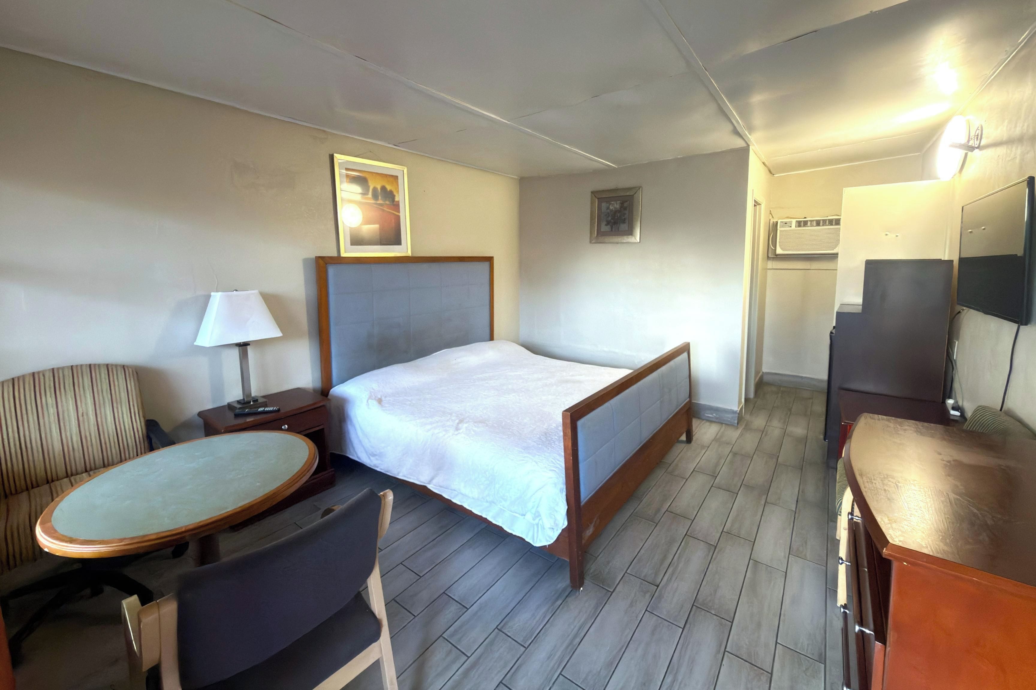 Una habitación de hotel con una cama, un escritorio con una silla, una mesita, una lámpara y un televisor.