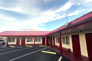 Un motel con techo rojo, varias habitaciones y estacionamiento.