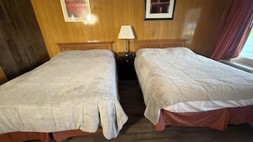 Une chambre d’hôtel avec deux lits, des lambris en bois aux murs, une table de chevet avec une lampe et des tableaux encadrés accrochés au mur.