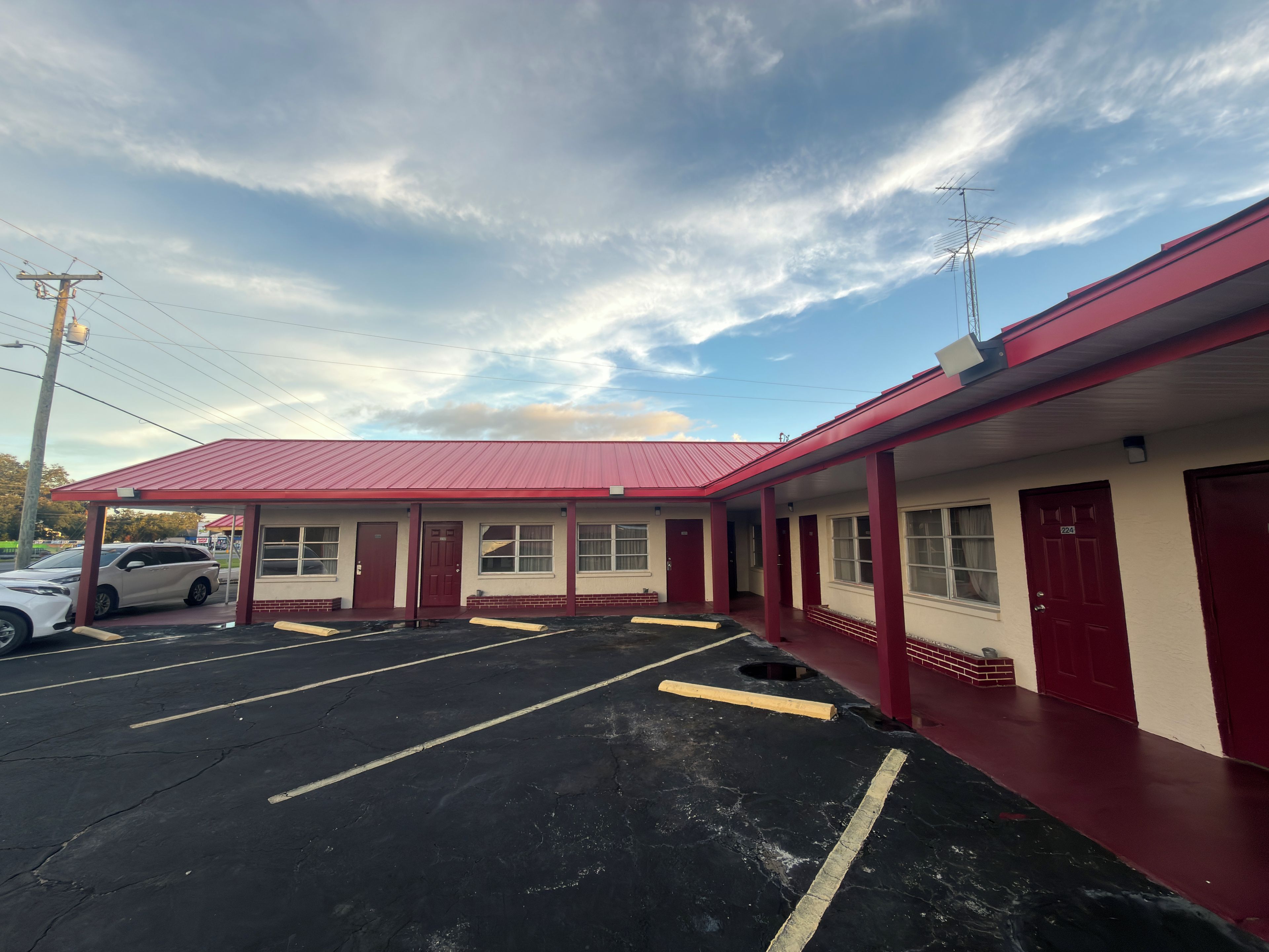 A motel with a red exterior, a parking lot, and a clear sky.