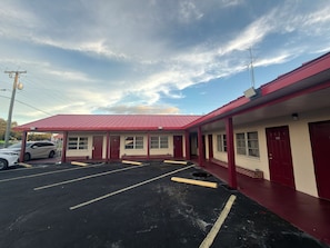 Un motel à l’extérieur rouge, avec un parking et un ciel dégagé.