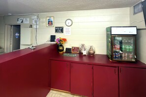 A reception desk with a clock, framed certificates, and a refrigerator stocked with beverages.