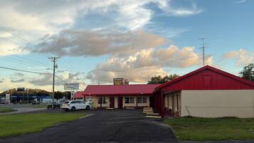 Un motel avec un toit rouge, un parking et un ciel dégagé parsemé de nuages.