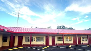 A motel with a red roof and multiple rooms, a parking lot, and a clear sky.