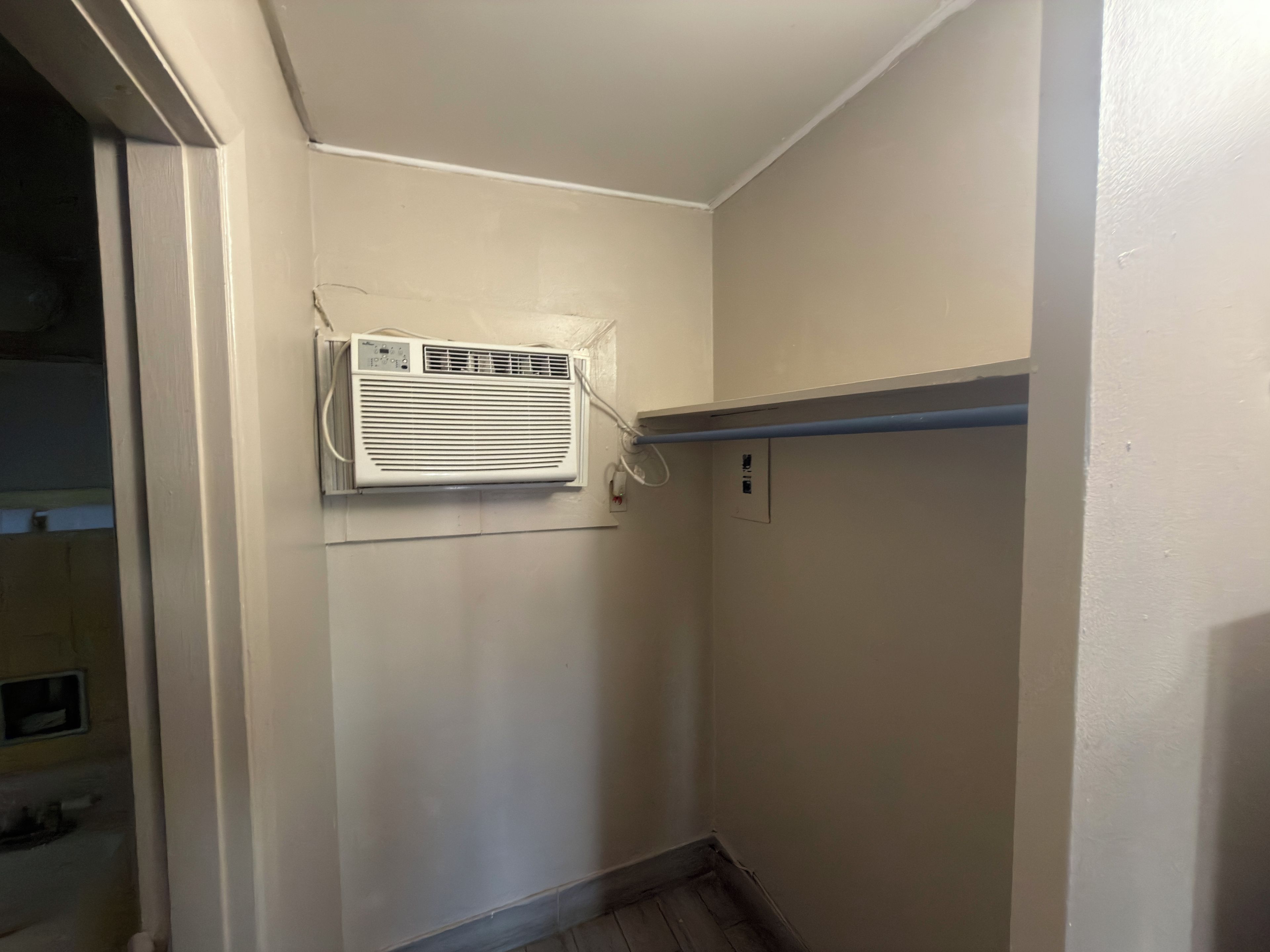 Un pasillo estrecho con pared blanca, un equipo de aire acondicionado instalado en el techo y un zócalo azul horizontal.