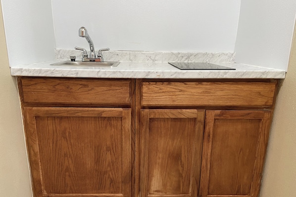 A kitchen with a single sink, wooden cabinets, and a marble countertop.