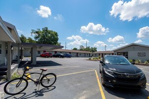 Un parcheggio con una bicicletta, un'auto e un edificio motel dotato di area di parcheggio coperta.