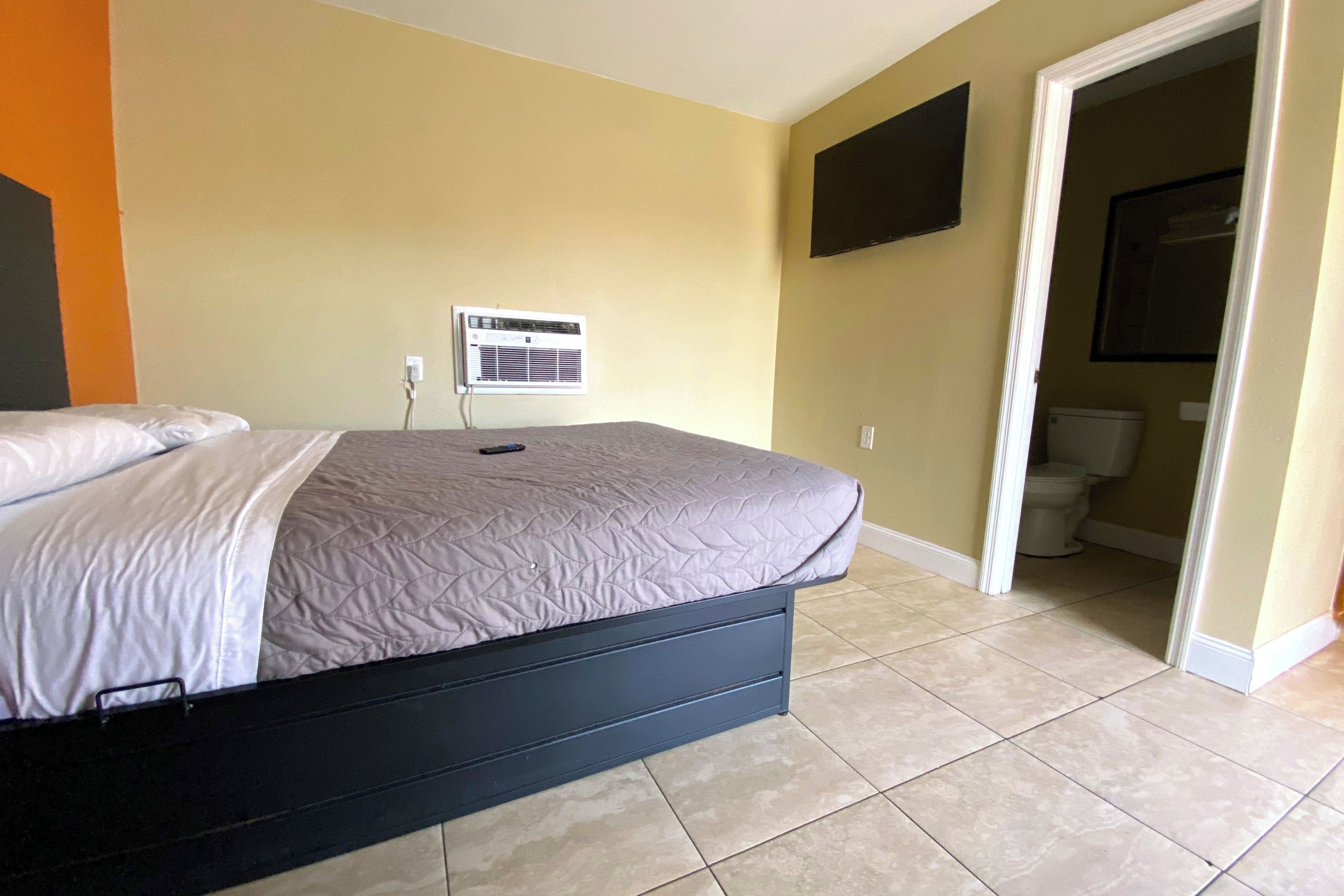 Un dormitorio con una cama, aire acondicionado de pared y una puerta que da a un baño.