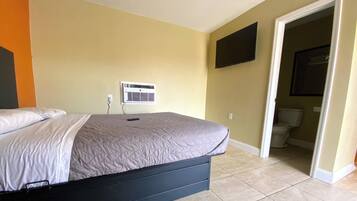 Un dormitorio con una cama, aire acondicionado de pared y una puerta que da a un baño.