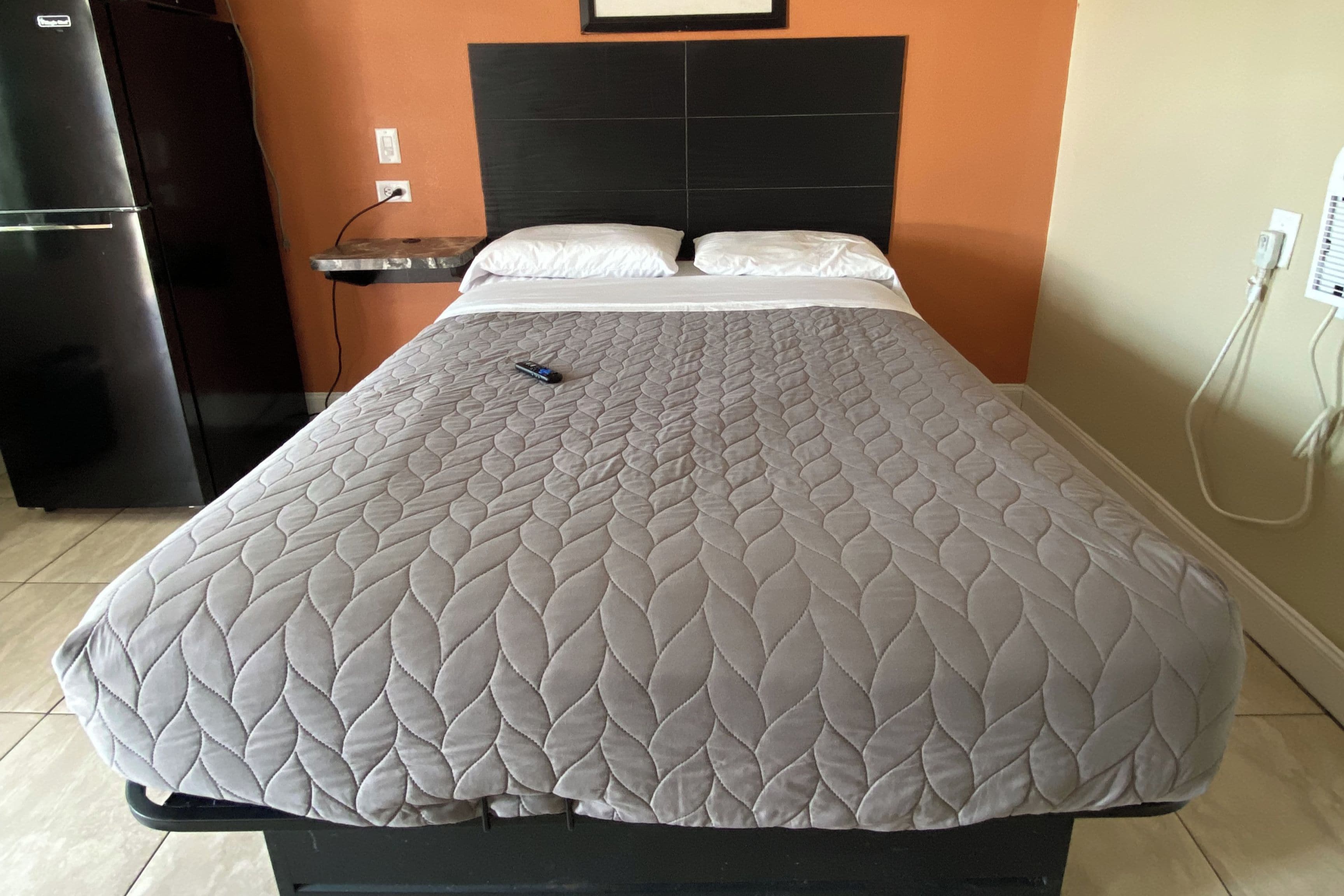 A bed with a quilted headboard, a bedside table, and a power outlet on the wall.