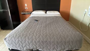 A bed with a quilted headboard, a bedside table, and a power outlet on the wall.