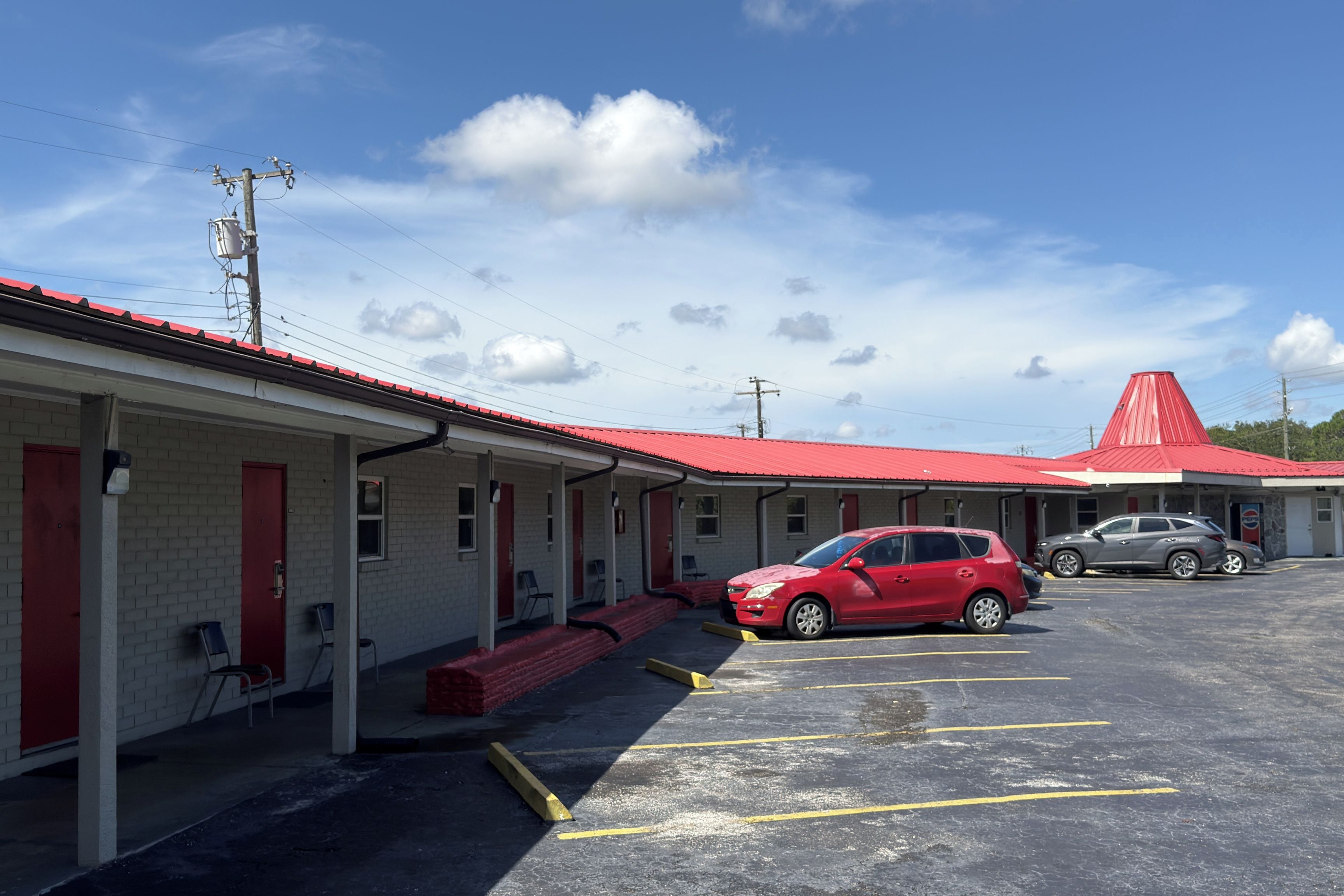 Un motel con techo rojo, un estacionamiento y dos coches aparcados.