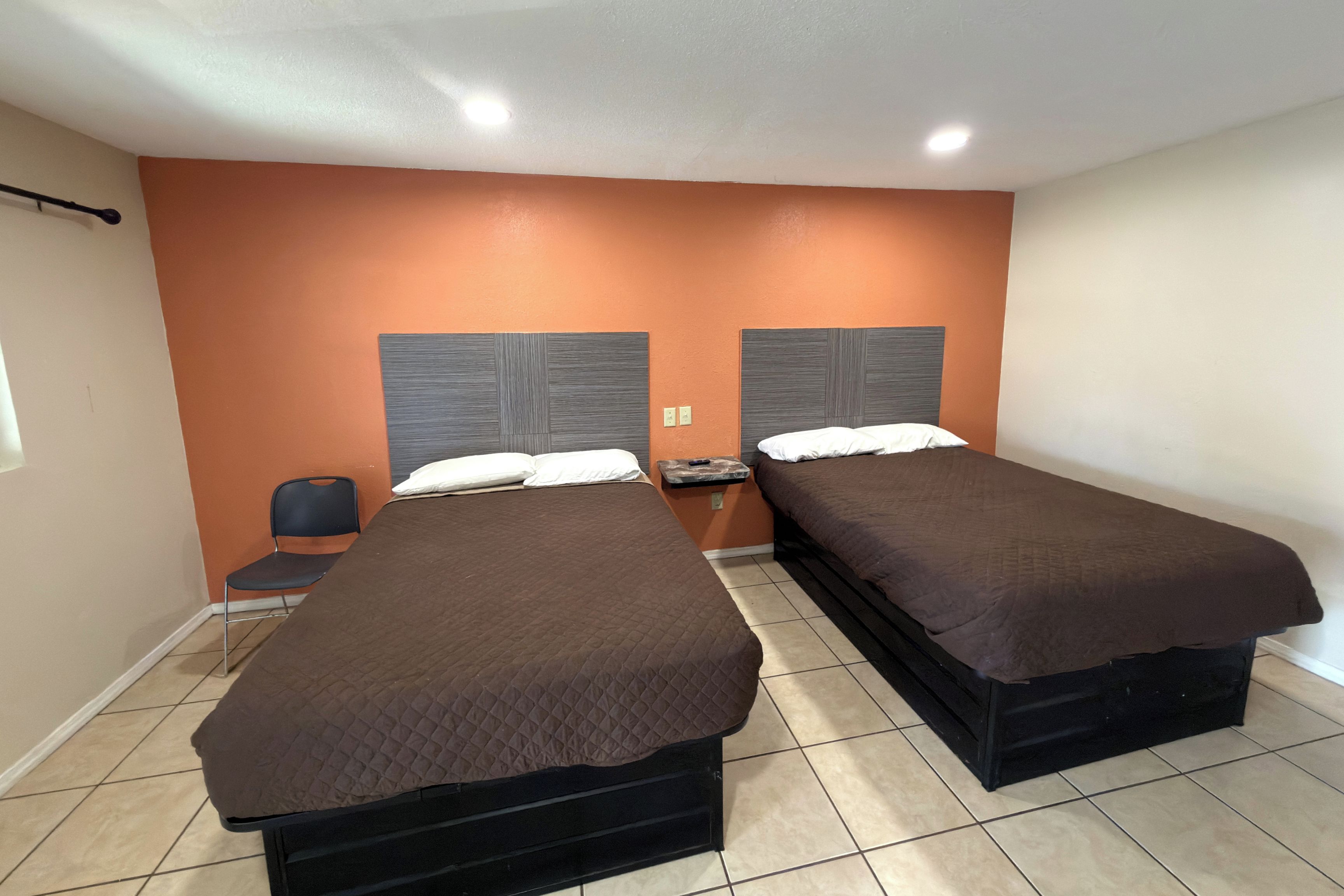 Habitación de hotel con dos camas, una silla y una mesita de noche.