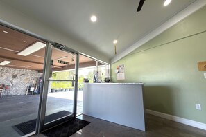 Zona de recepción con entrada por puerta de vidrio, mostrador de recepción y pared de piedra con letrero de Pepsi.
