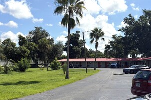 Un motel con techo rojo, coches aparcados y una zona verde con árboles.