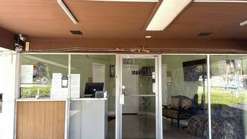 Zona de recepción con mostrador, computadora y área de descanso con sofá y sillones.