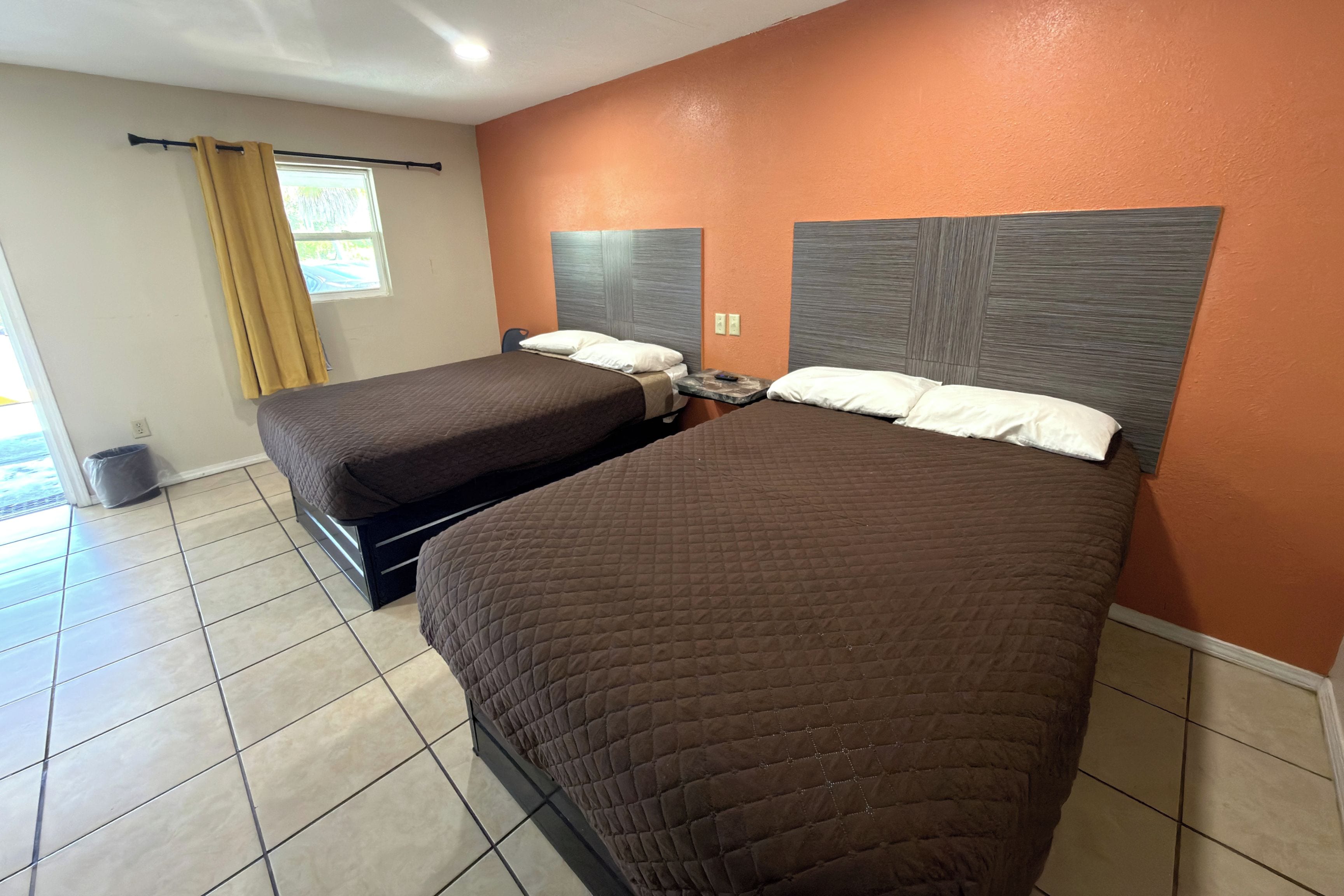 A hotel room with two beds, a window with curtains, and a tiled floor.