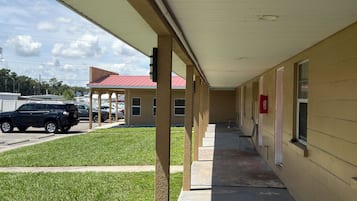 A covered outdoor area with a building in the background, a parking lot, and a grassy area.