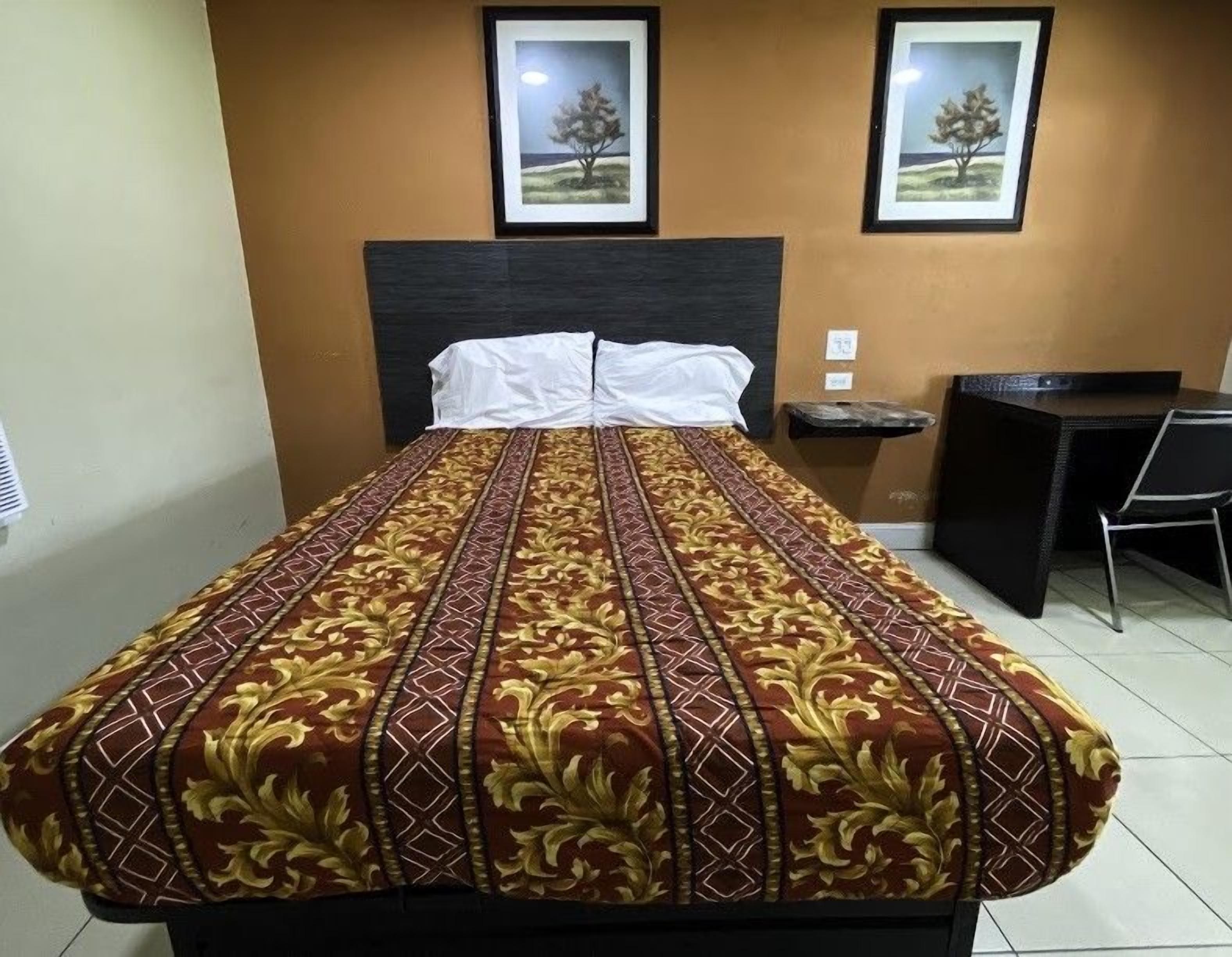 A hotel room with a bed, a desk, and two framed pictures on the wall.