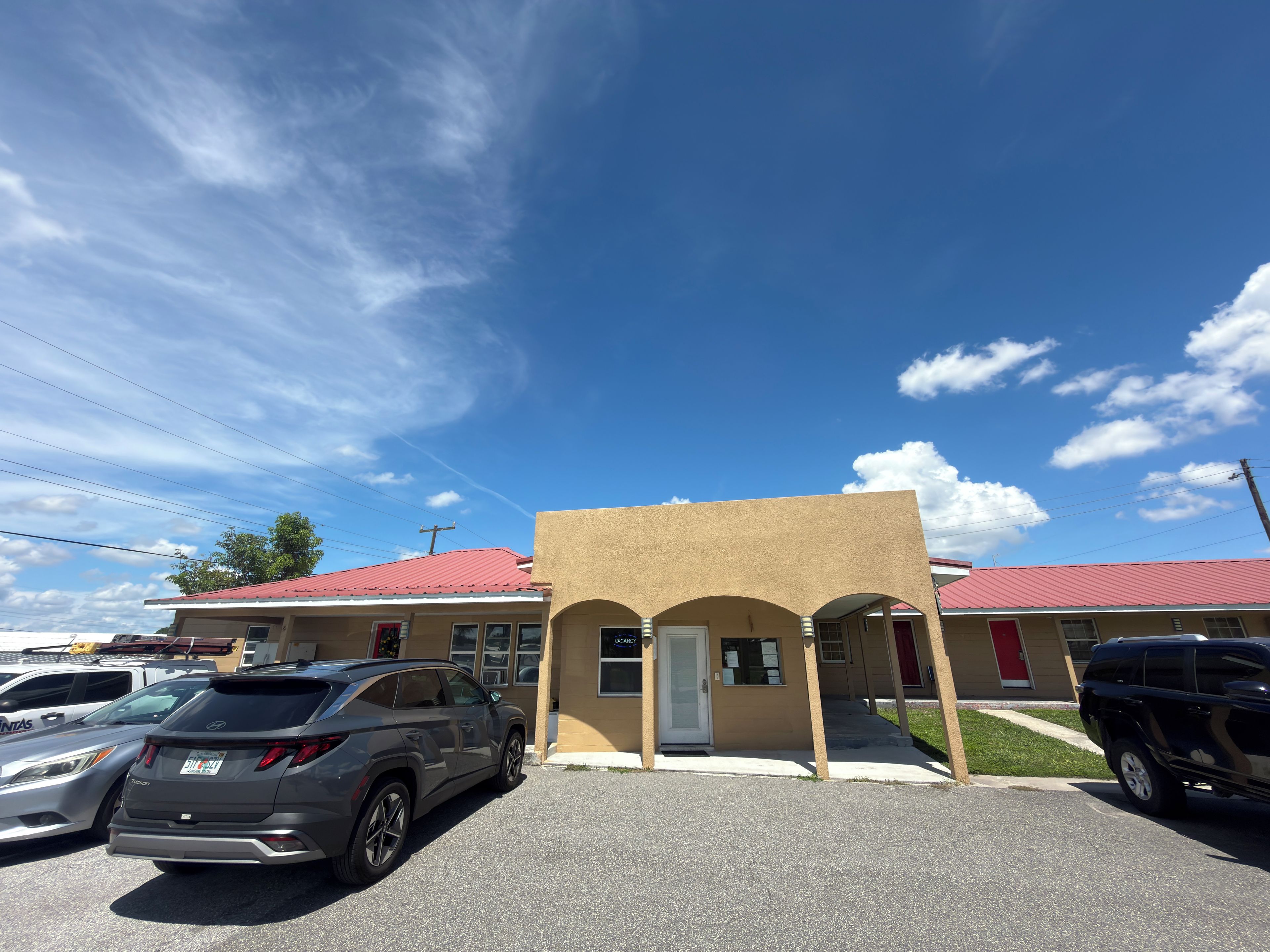A parking lot with several SUVs, a building with a red roof, and a clear blue sky.