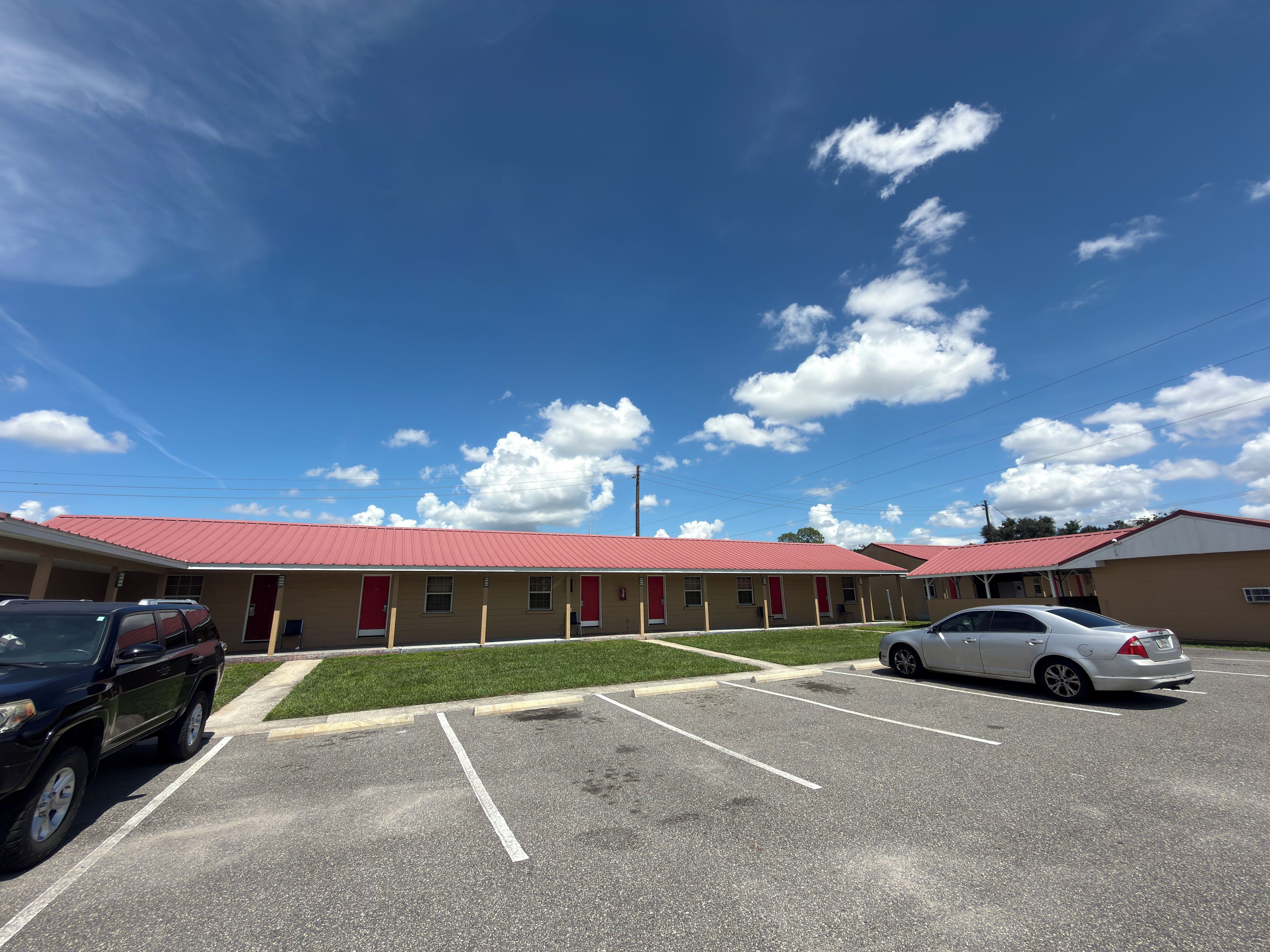 A motel with a red roof, multiple rooms, and a parking lot.