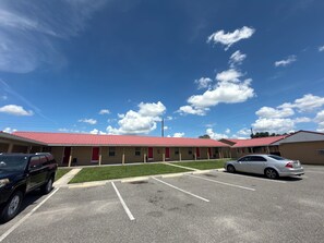 A motel with a red roof, multiple rooms, and a parking lot.