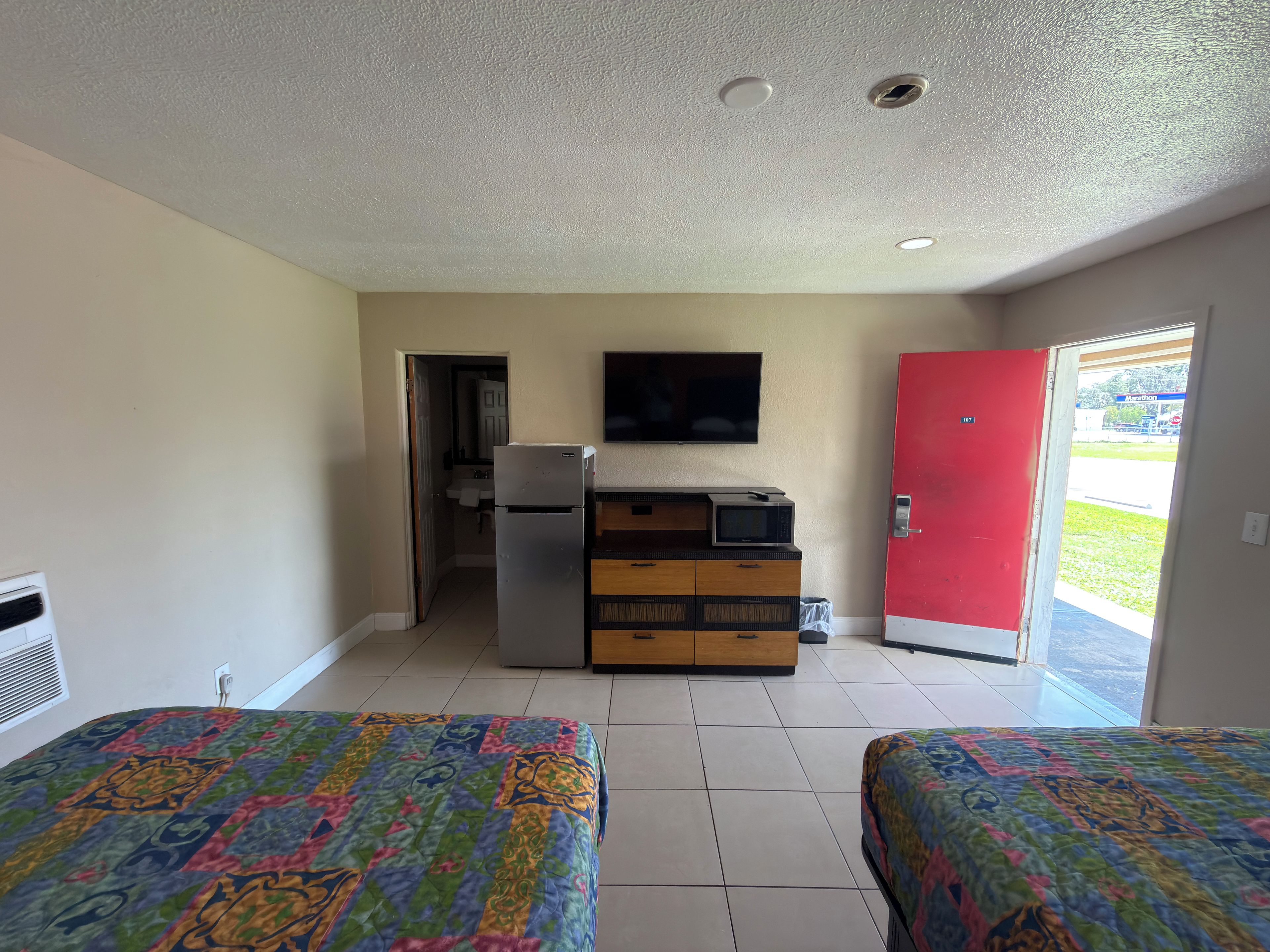 Una habitación con dos camas, kitchenette, televisor y una puerta roja.