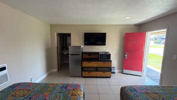 Una habitación con dos camas, kitchenette, televisor y una puerta roja.