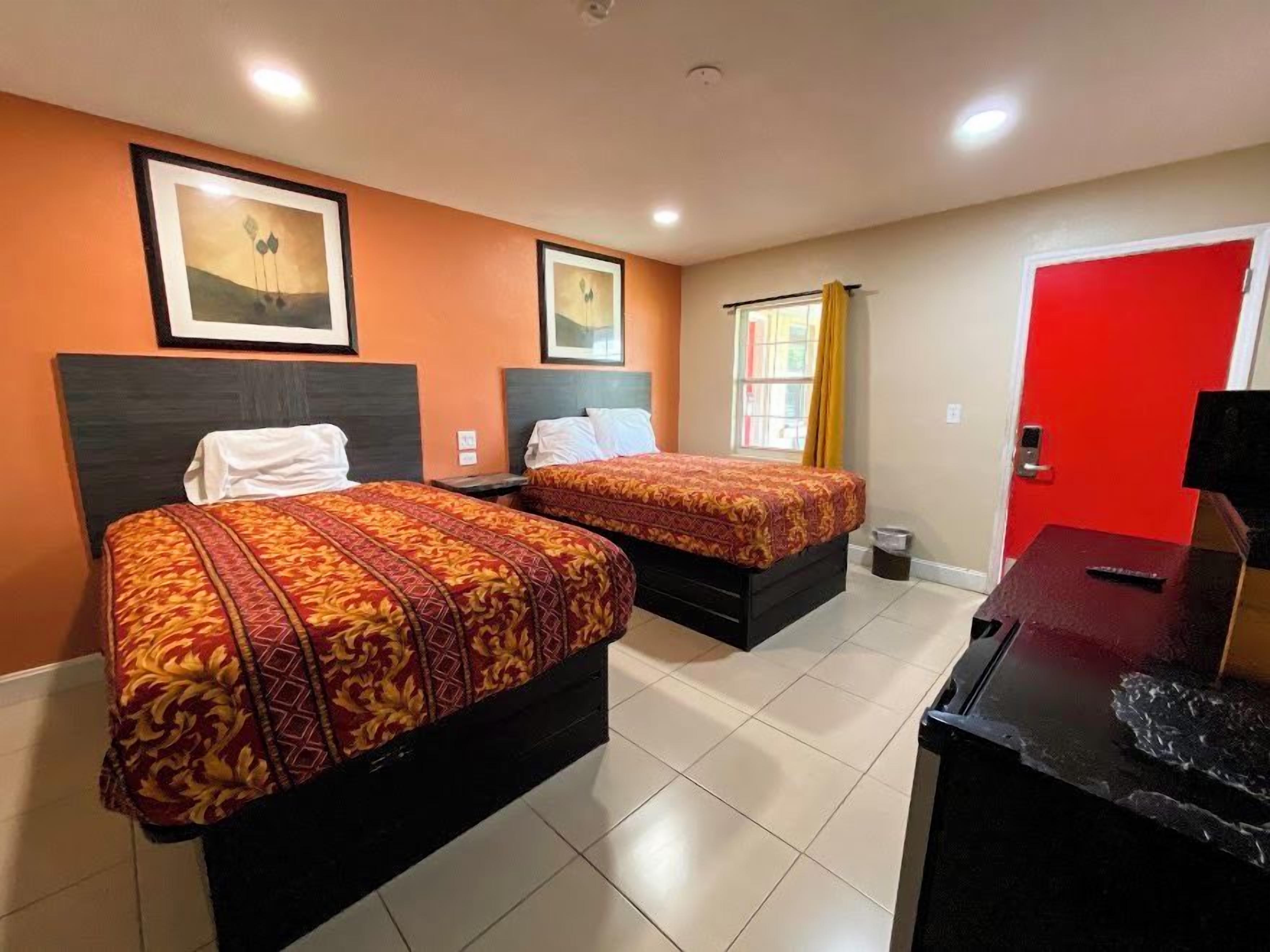 A hotel room with two beds, a red door, and a window with curtains.