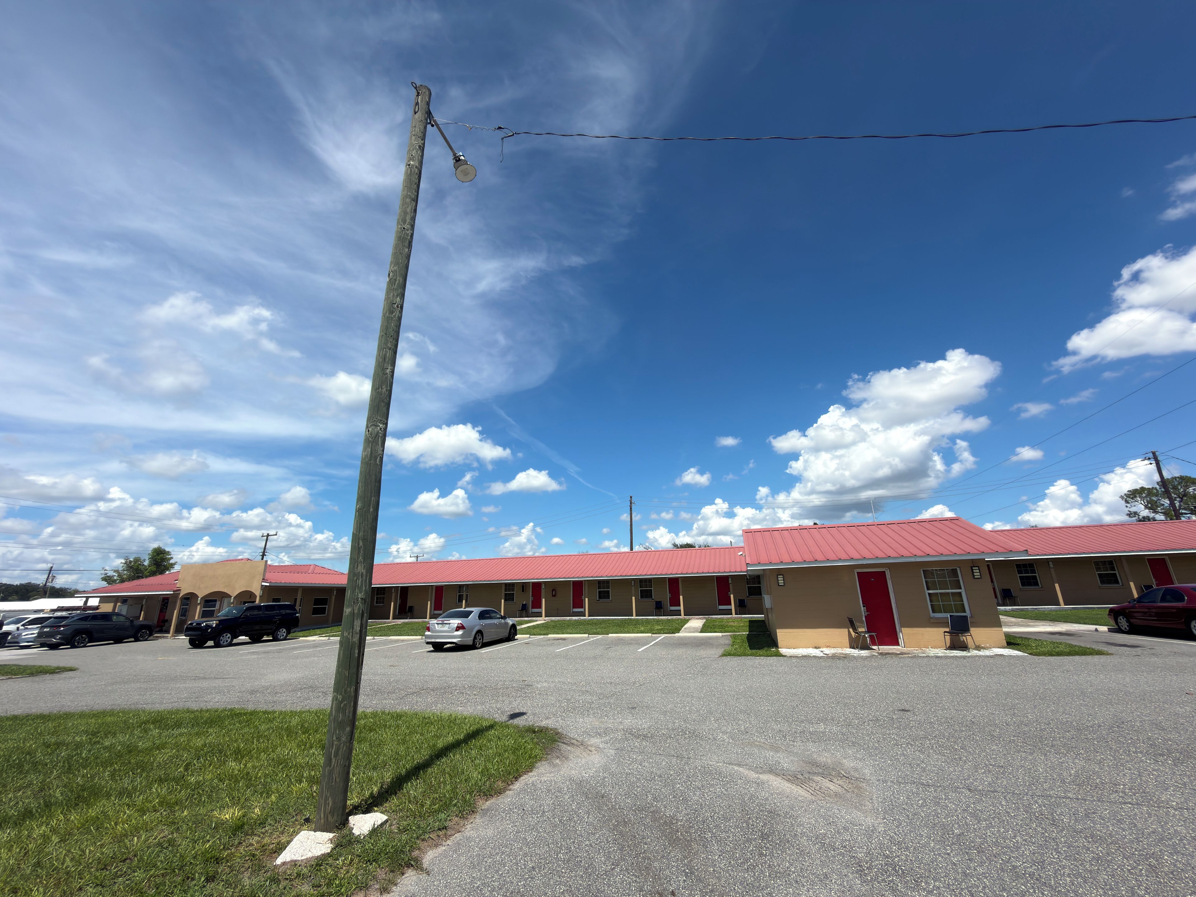 Un motel con techo rojo, varias habitaciones y estacionamiento.