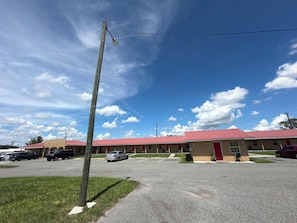 A motel with a red roof, multiple rooms, and a parking lot.