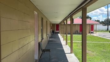 Un corredor cubierto con una fila de sillas individuales, una puerta roja y un edificio pequeño con techo rojo al fondo.