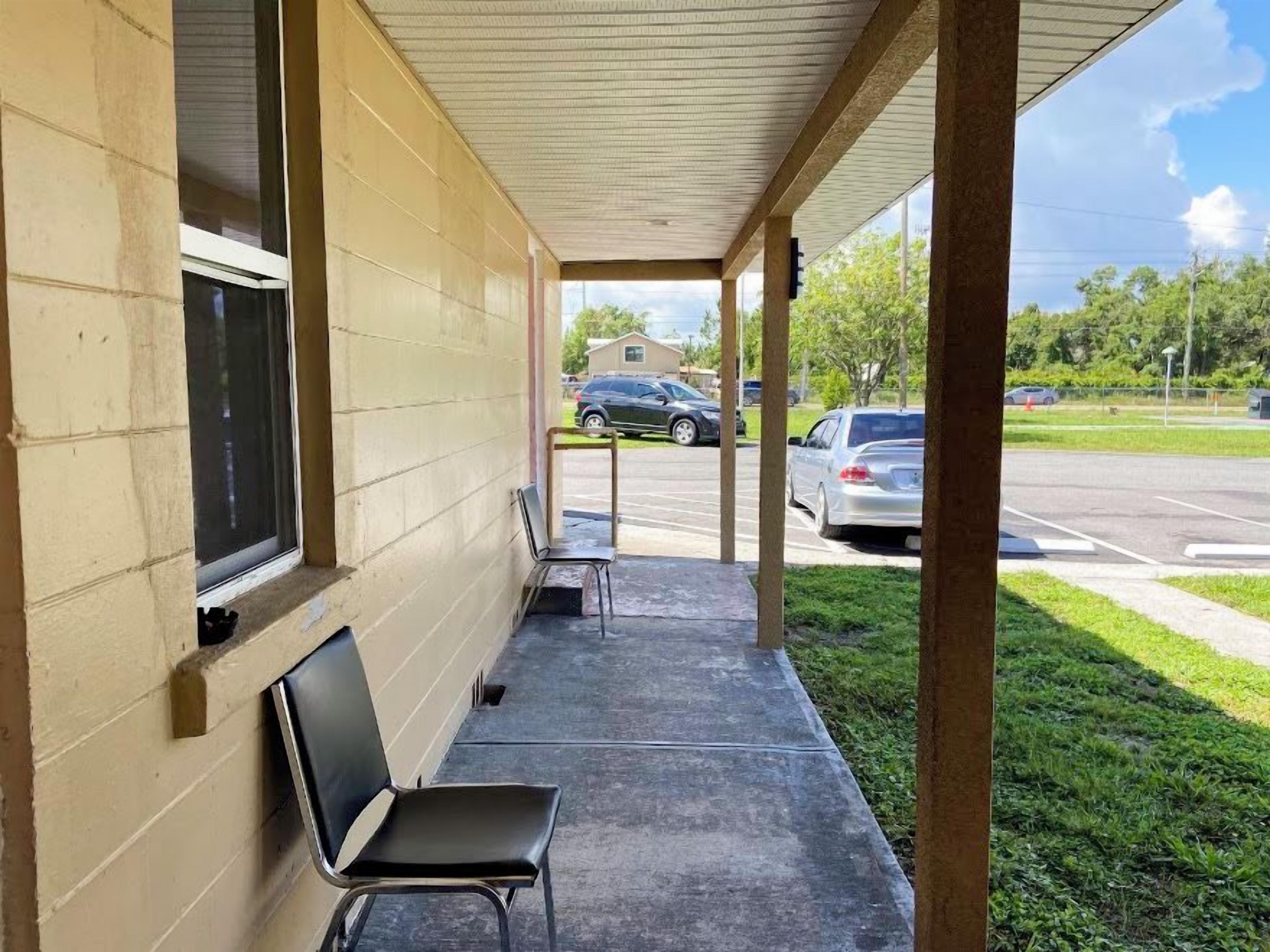 A covered outdoor area with a bench and a window, a parking lot with cars, and a grassy area.
