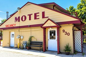 Un motel con un cartel de 'VACANCY', un banco y una puerta con la leyenda 'OFICINA'.