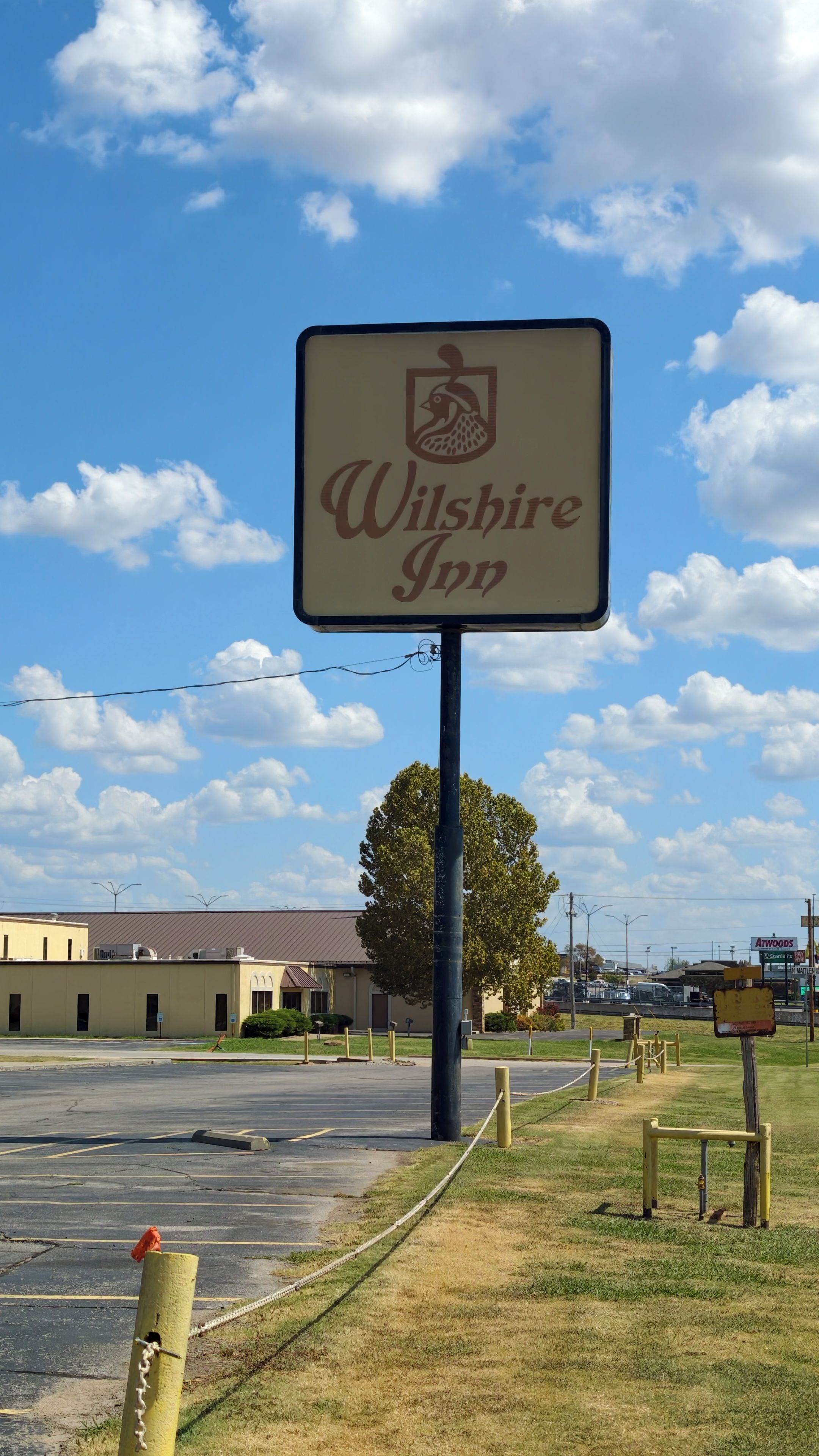 Letrero del Wilshire Inn con un logotipo, sobre un cielo despejado con nubes.