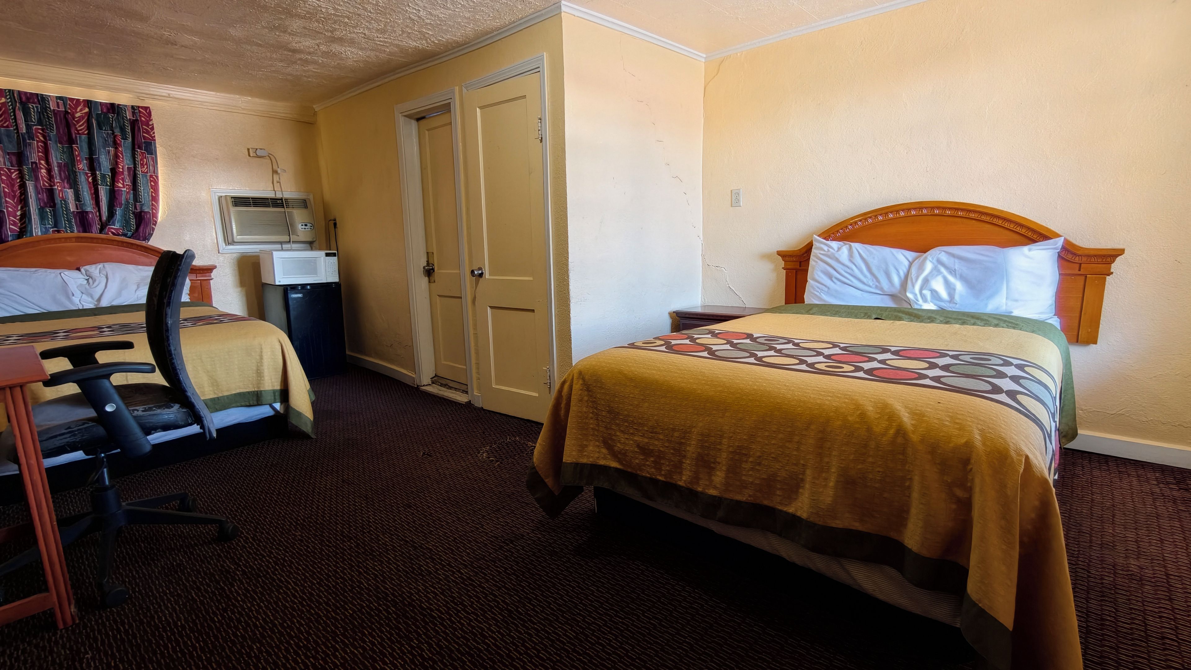Habitación de hotel con dos camas, un escritorio con silla, microondas y armario.