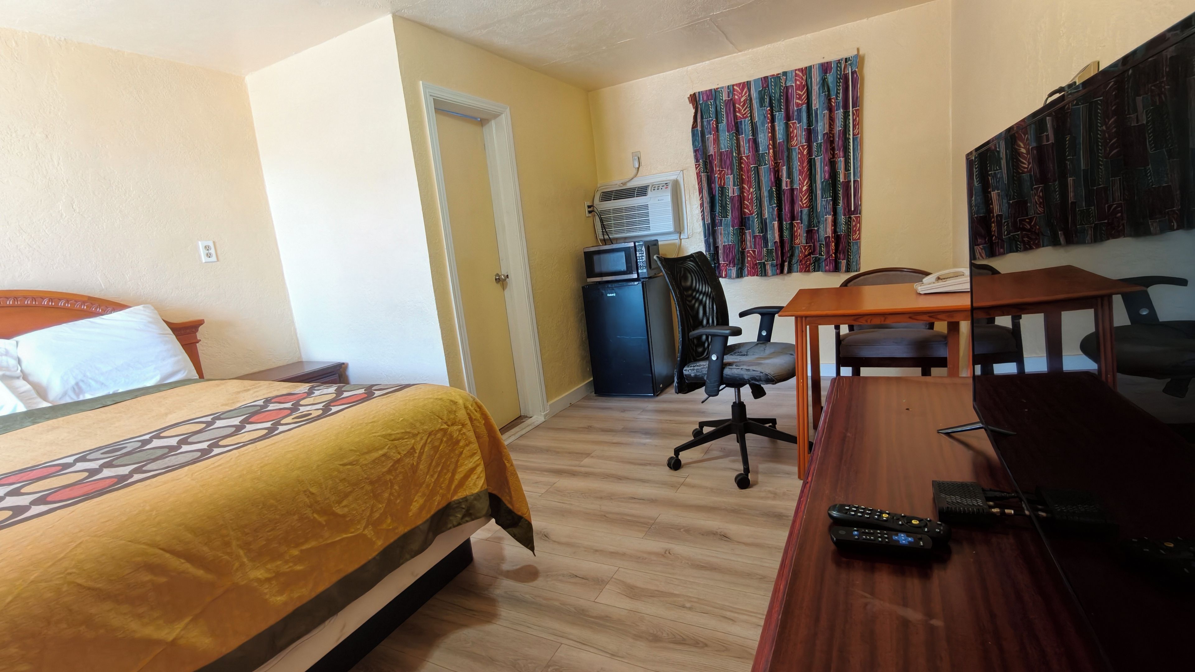 Habitación de hotel con cama, escritorio, silla, microondas y televisor.