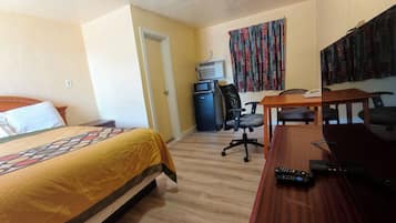 Habitación de hotel con cama, escritorio, silla, microondas y televisor.