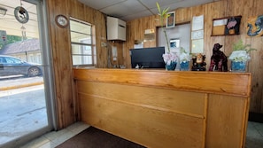 A reception desk with a wooden finish, a television, and various decorative items including flowers and figurines. - La-Ze L Motel Cushing OK (Cushing)