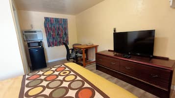 A hotel room with a bed, a desk, a television, a refrigerator, and a patterned rug.