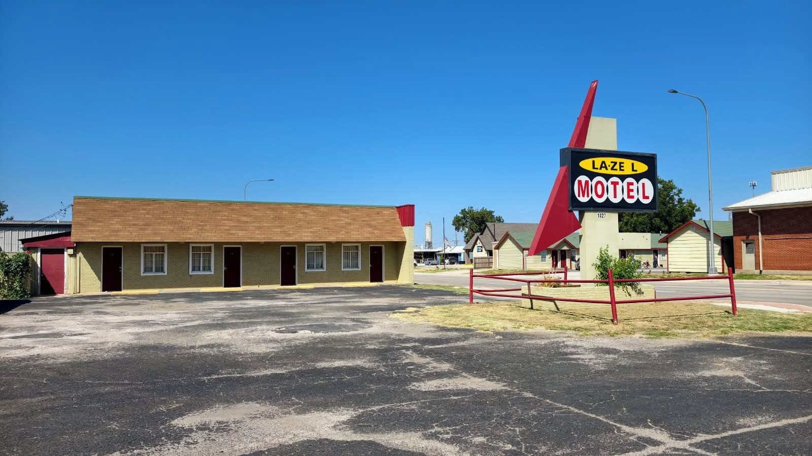 A motel with a distinctive red and yellow sign, a parking lot, and a building with multiple doors.
